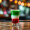 Bicchierino di Mexican Flag chupito perfettamente stratificato con verde, bianco e rosso su bancone di bar, decorato con sombrero e dettagli festosi in stile messicano sullo sfondo.